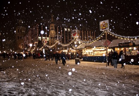 Besneeuwde straat met kraampjes van een kerstmarkt en enkele bezoekers