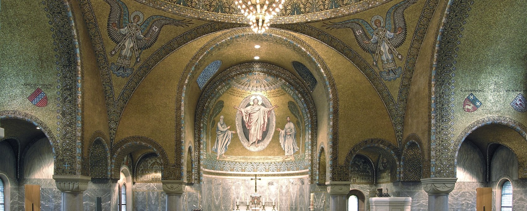 Das Innere der Erlöserkirche mit Blick zur Decke und zum Altar. Die Decke ist mit goldenen Mosaiken, Engeln und einem großen Kronleuchter geschmückt. Rundfenster lassen Licht in den prunkvollen Kirchenraum.