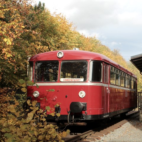 Eine historische rote Eisenbahn mit Schild &quot;Sonderfahrt&quot; parkt auf Schienen neben einem alten Bahnhofsgebäude bei Herbstwetter.
