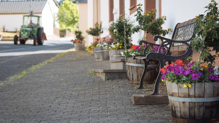 Eine gemütliche Straße mit einer Bank und Blumenkübeln. Im Hintergrund ist ein Traktor zu sehen.