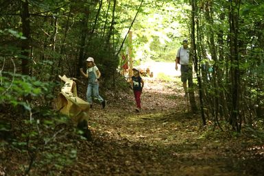 Zwei Kinder laufen auf einem Waldweg neben einer Kugelbahn aus Holz.