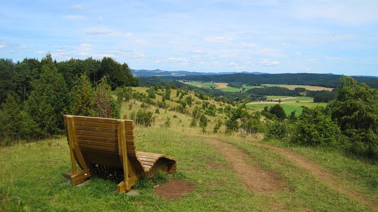 Holzbank auf einem Hügel mit Blick auf eine weite Landschaft und Wälder am Hönselberg.