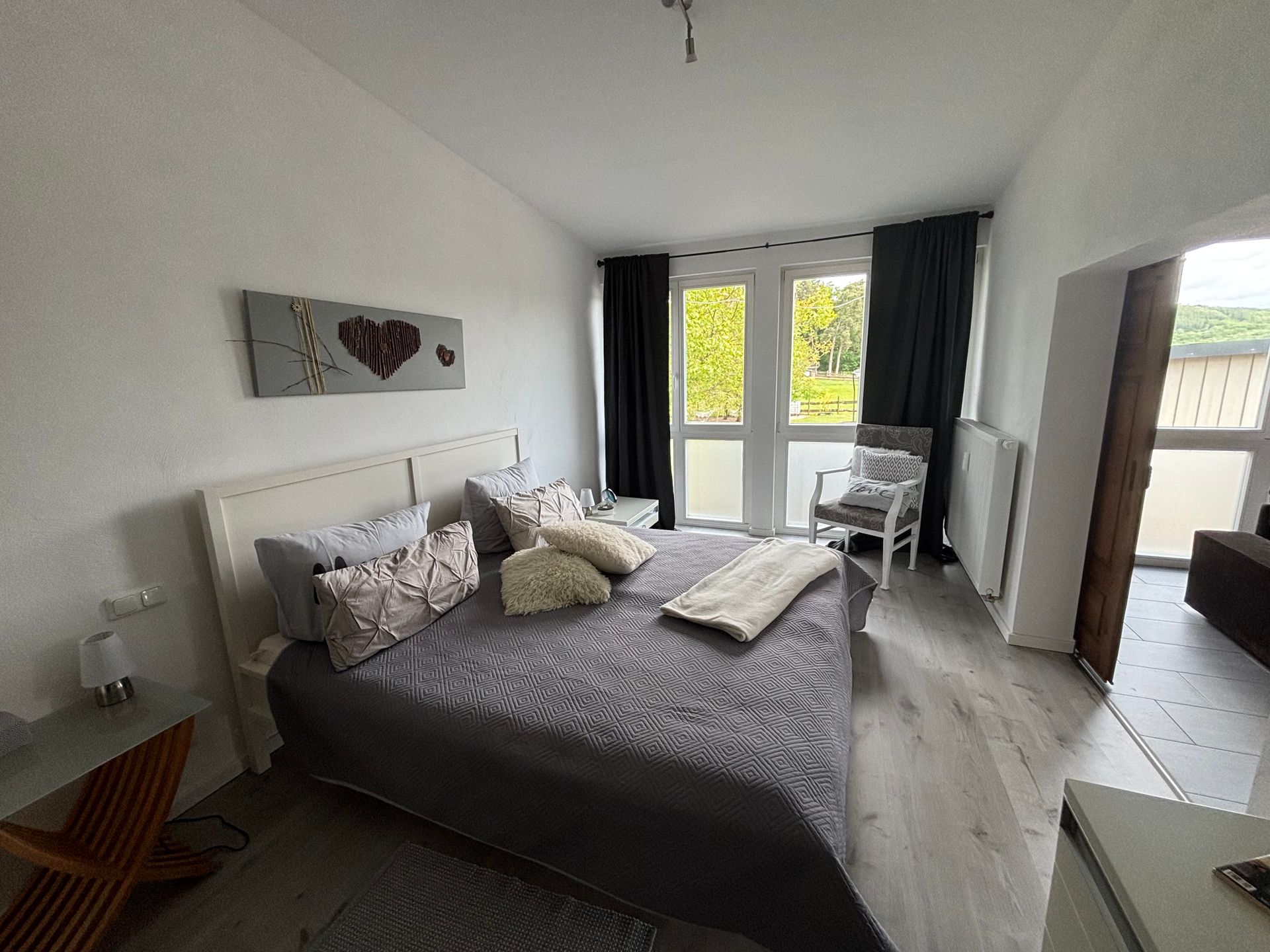 Ein offenes Schafzimmer mit einem großen Doppelbett mit Dekokissen darauf und einem großen Fenster dahinter.