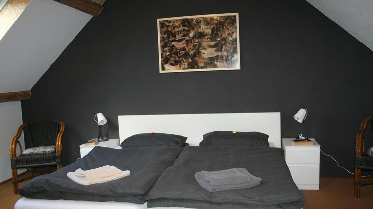 Een gezellige slaapkamer met twee bedden en een donker wandontwerp. Een afbeelding hangt boven het bed, en er is een nachtkastje naast elk bed.
