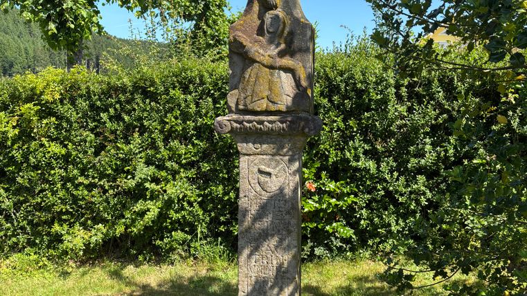 Stone crucifix in a garden with trees in the background.