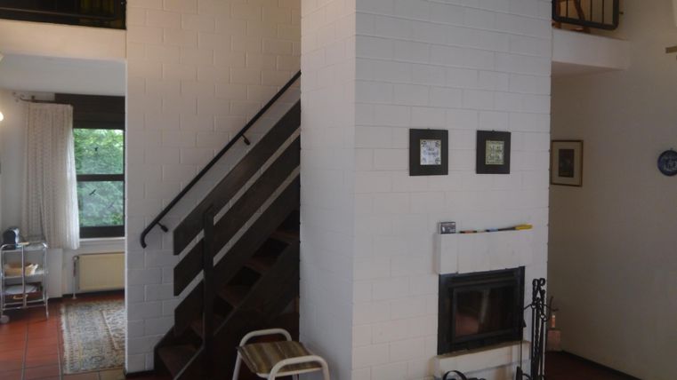 Ein helles Wohnzimmer mit einem gemütlichen Holzofen und einer Treppe. Es gibt große Fenster, die eine gute Sicht nach draußen bieten.