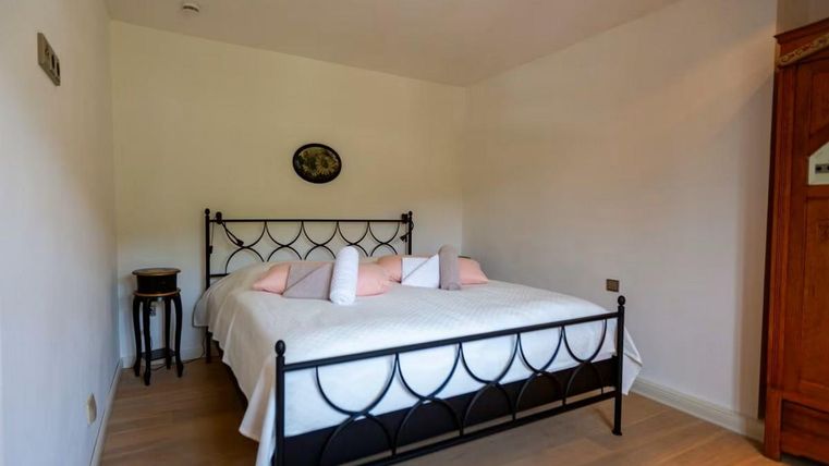 Ein einfaches Schlafzimmer mit einem schwarzen Metallbett und weißen Bettwäsche. An der Wand hängt ein kleines Bild, und es gibt einen Holzschrank sowie einen Beistelltisch.