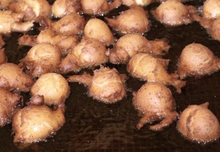 Close-up of numerous dough balls being fried in fat.