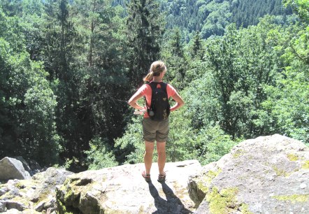 Eine Person steht auf einem Felsen und blickt auf ein dicht bewaldetes Tal. Sie trägt einen Rucksack und genießt die Aussicht., © Touristik GmbH Gerolsteiner Land, Ute Klinkhammer