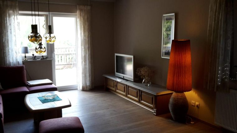 A modern living room with a large window and plenty of natural light. There is a cozy seating area, a television, and a stylish floor lamp.