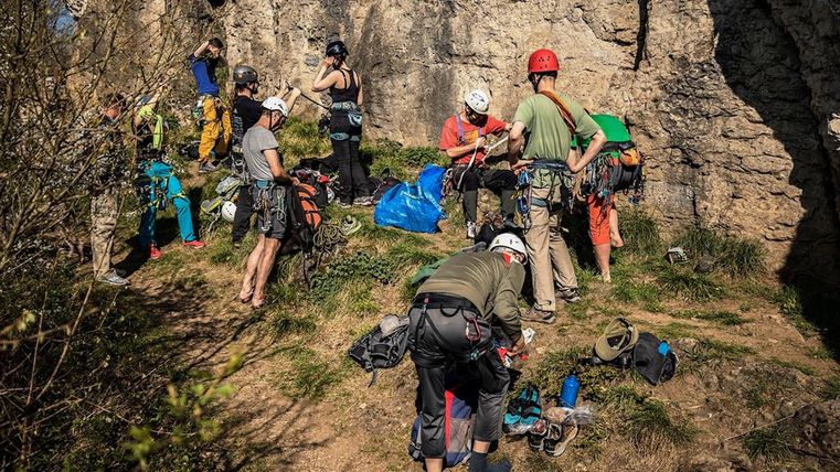 Eine Gruppe von Kletterern rüstet sich an einer Felswand aus. Sie tragen Helme und Kletterausrüstung, um sich auf das Klettern vorzubereiten.