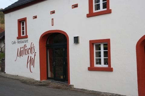Weißes Gebäude mit roten Fensterrahmen und der Aufschrift 'Müllisch's Hof'. Eingangstür in dunklem Holz.