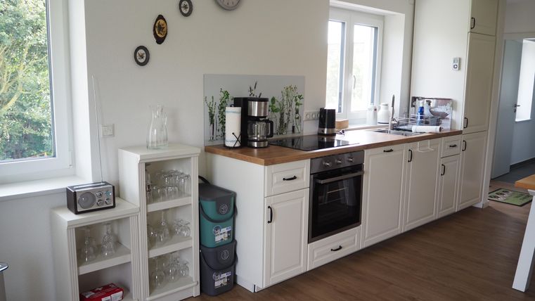 Eine helle und moderne Küche mit Holzoberflächen und großen Fenstern. Auf der Arbeitsplatte stehen ein Kaffeeautomaten und verschiedene Küchengeräte.