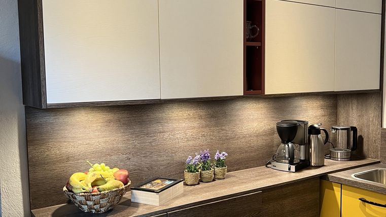 Een moderne keuken met hangkasten in lichte en donkere kleurtinten. Op het aanrecht staan een fruitschaal en keukenapparatuur.