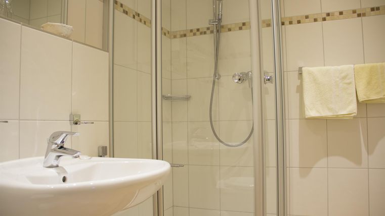 Ein modernes Badezimmer mit einer Duschkabine und einem Waschbecken. Hell geflieste Wände verleihen dem Raum eine angenehme Atmosphäre.