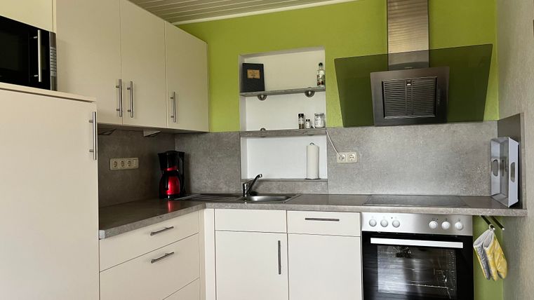 Eine moderne Küche mit weißen Schränken und einer grünen Wand. Sie ist ausgestattet mit einem Herd, einem Kühlschrank und einer Edelstahlabzugshaube.