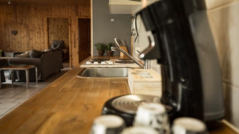 Eine moderne Küche mit einem Holzarbeitsplatz, einer Kaffeemaschine und zwei Spülen. Im Hintergrund sind gemütliche Möbel zu sehen.