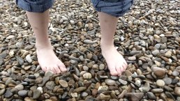 Two bare feet are standing on a pebble beach. The person is wearing rolled-up jeans., © pixabay