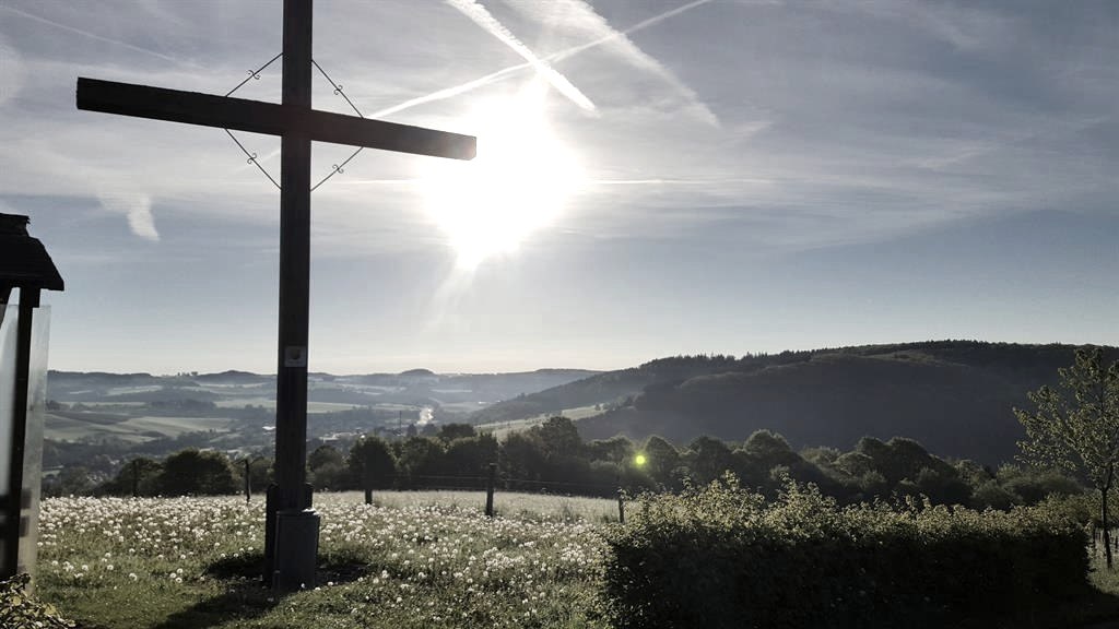 Holzkreuz auf einer Wiese, im Hintergrund die hügelige Landschaft der Eifel bei Sonnenaufgang., © Touristik GmbH Gerolsteiner Land