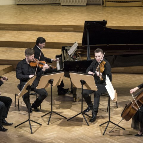 Four string players and a pianist perform together on stage.
