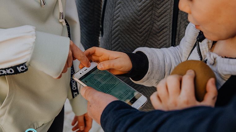 Kinder interagieren mit einem Smartphone während einer Schatzsuche.
