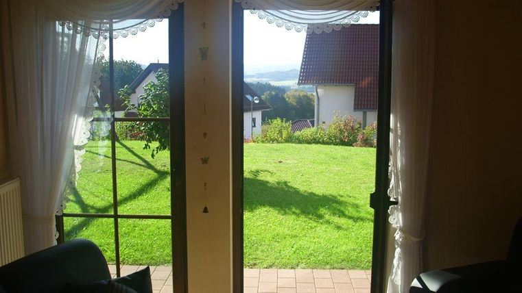 Ein offenes Fenster mit Blick auf einen grünen Garten. Im Hintergrund sind Häuser und ein klarer Himmel zu sehen.