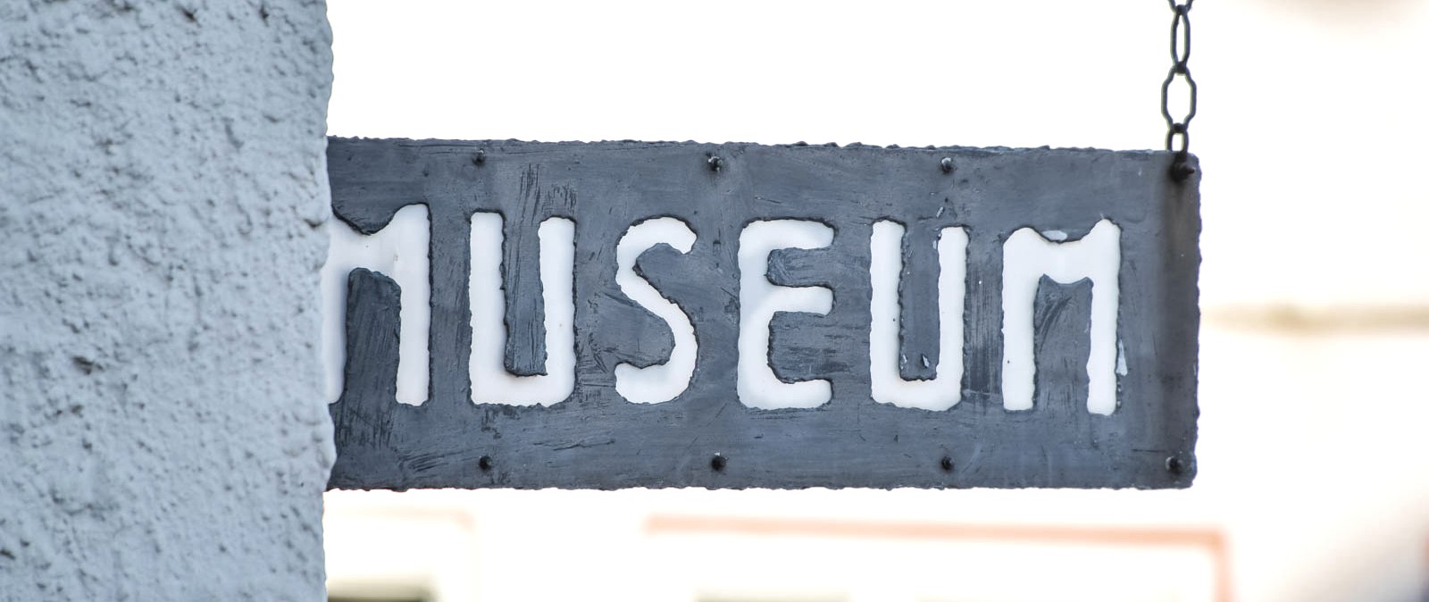 Nahaufnahme eines grauen Schildes mit Schriftzug "Museum" an einer Hauswand.