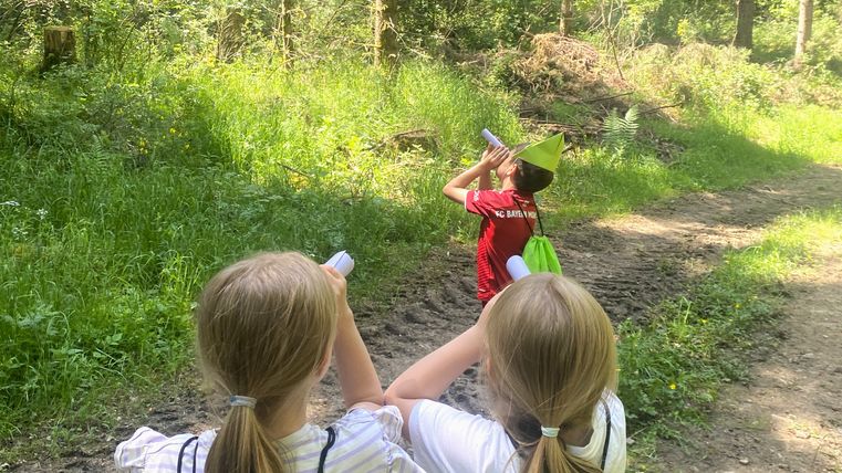 Drei Kinder im Wald, die durch Papierrollen schauen.