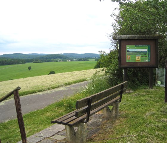Aussichtspunkt in Leudersdorf mit Bank und Infotafel. Weite grüne Felder und bewaldete Hügel im Hintergrund., © Touristik GmbH Gerolsteiner Land, Ute Klinkhammer