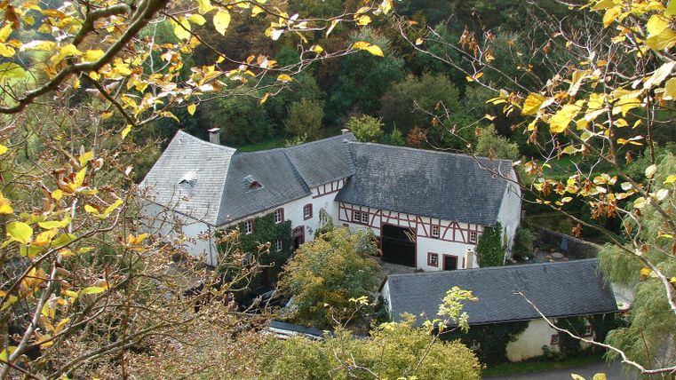 A traditional half-timbered house surrounded by trees and autumn leaves. The quiet rural setting conveys a peaceful atmosphere.