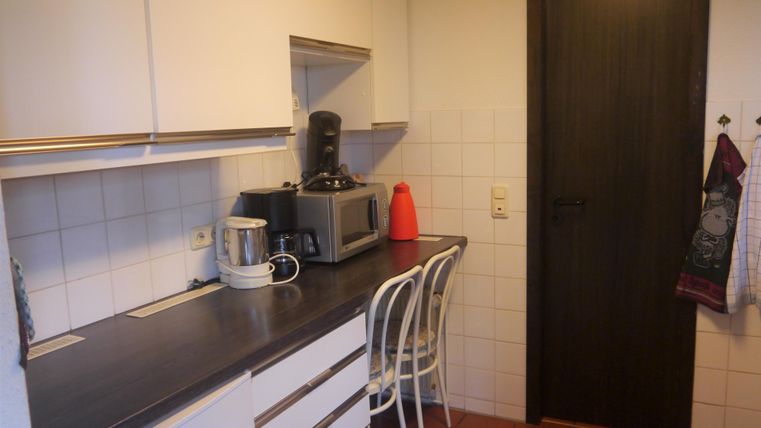 Eine moderne Küche mit weißen Schränken und einem Holzfußboden. Auf der Arbeitsplatte stehen Küchengeräte und ein roter Wasserkocher.