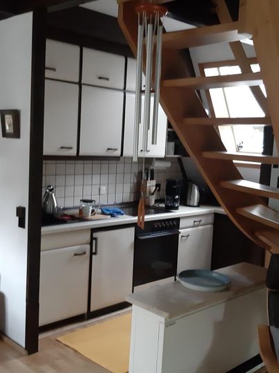 Eine kleine, moderne Küche mit Holzelementen und einer Wendeltreppe. Der Raum wirkt hell und einladend.