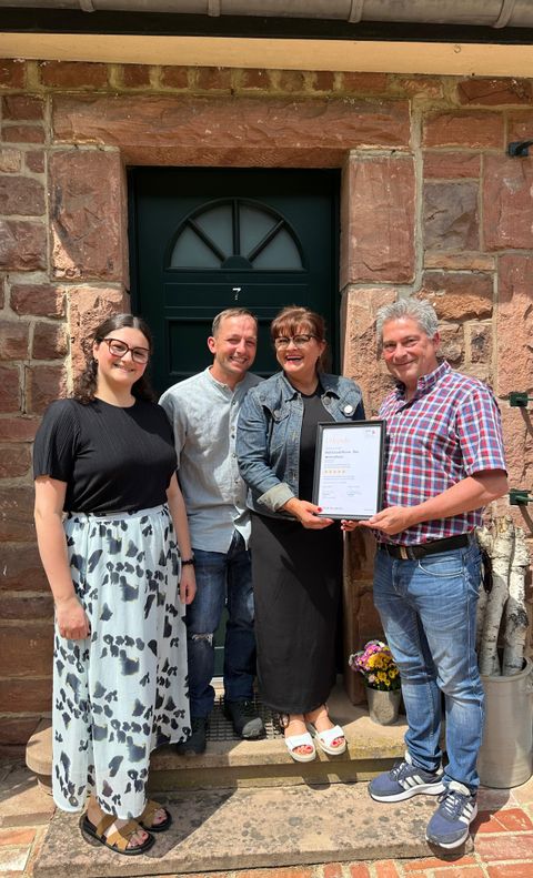 Vier erfreute und lachende Personen stehen vor einer Eingangstür und halten Stolz die Urkunde für die Klassifizierung in den Händen.