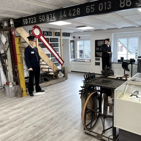 Ausstellungsraum eines Museums zum Thema Eisenbahngeschichte mit Puppen in Schaffneruniform, Schranken, Plaketten und vieles mehr.