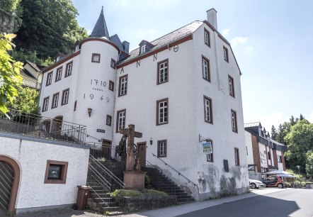 Historic building in Gerolstein with the inscriptions &ldquo;Anno 1710&rdquo; and &ldquo;1949&rdquo;, stairs and statue in the foreground, blue sky in the background.