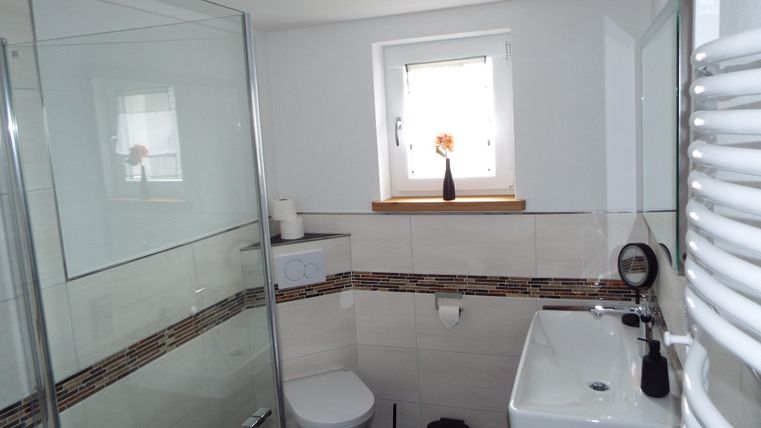 Ein modernes Badezimmer mit einer Glasdusche und hellem Fliesenboden. Ein kleines Fenster lässt natürliches Licht hereinfällt.