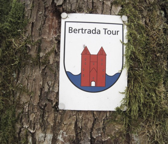 Bertrada Tour bord met rood torenlogo, bevestigd aan een boomstam met mosgroei., &copy; Touristik GmbH Gerolsteiner Land, Ute Klinkhammer