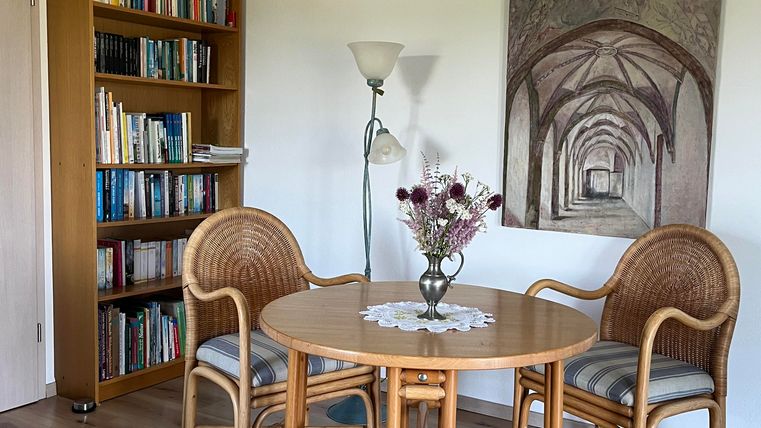 Une pièce confortable avec une table ronde et deux chaises.
À l'arrière-plan, il y a une étagère et un tableau est accroché au mur.