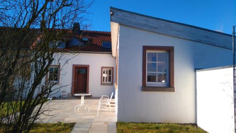 Une maison moderne avec un espace extérieur lumineux et un coin salon. Le ciel est clair et bleu.