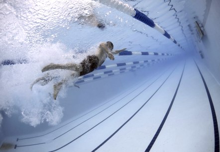 Underwater shot of a swimmer wearing swimming trunks, a swimming cap and diving goggles swimming a length underwater. 