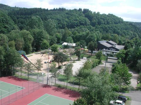 Freizeitpark mit Tennisplatz, Spielplatz und Restaurant in bewaldeter Umgebung. Im Hintergrund dichte Wälder, im Vordergrund Sport- und Spielanlagen.
