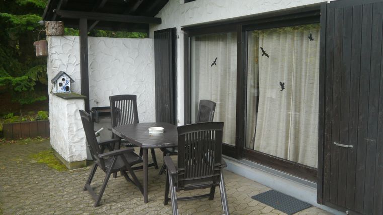 Ein gemütlicher Außenbereich mit einem Tisch und Stühlen. Die Türen sind geschlossen und eine Vogelfutterstation steht bereit.
