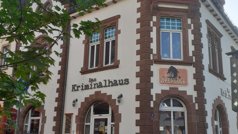 Historisches Gebäude mit der Aufschrift 'Das Kriminalhaus' und 'Café Sherlock', davor ein schwarzes Oldtimer-Auto.