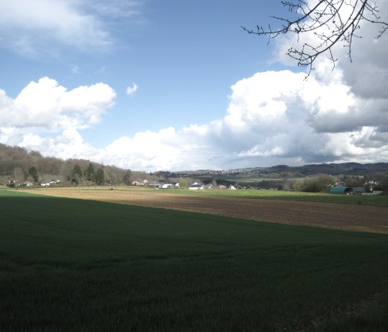 Weite Landschaft mit grünen Feldern und Wolken am Himmel, Blick auf das Dorf Oberbettingen in der Ferne., © Touristik GmbH Gerolsteiner Land, Ute Klinkhammer