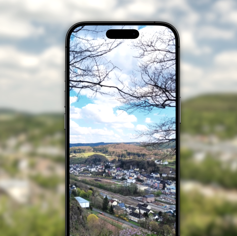 Vor dem verschwommenen Hintergrund ist ein Handy, welches ein Bild von Gerolstein von oben zeigt.