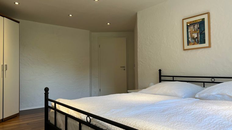 Een gezellige slaapkamer met een dubbelbed en een kledingkast. De muren zijn wit en er hangt een klein schilderij aan de muur.