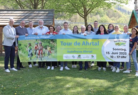 16 Personen stehen dicht beieinander, halten ein Banner f&uuml;r den Radaktionstag Tour de Ahrtal am Sonntag, 15. Juni 2025 hoch und l&auml;cherln in die Kamera.
