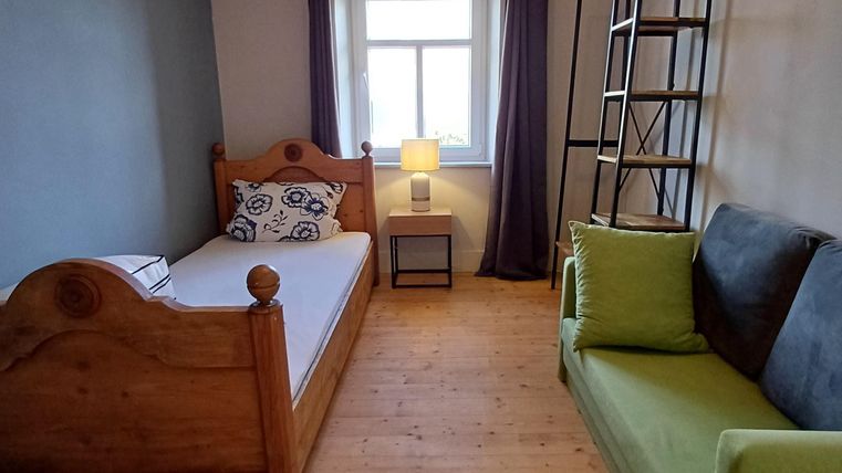 Een gezellige slaapkamer met een helder eenpersoonsbed en een groene bank. De kamer heeft een raam met uitzicht naar buiten en is uitgerust met een tafel en een lamp.