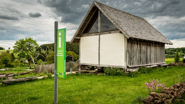 Ein Informationsschild vor einem historischen Gebäude in einer grünen Landschaft.