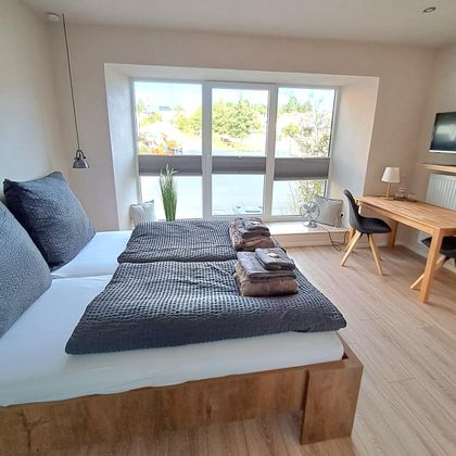 Ein helle und moderne Schlafzimmer mit zwei Betten und großen Fenstern. Der Raum verfügt außerdem über einen Schreibtisch und eine gemütliche Atmosphäre.